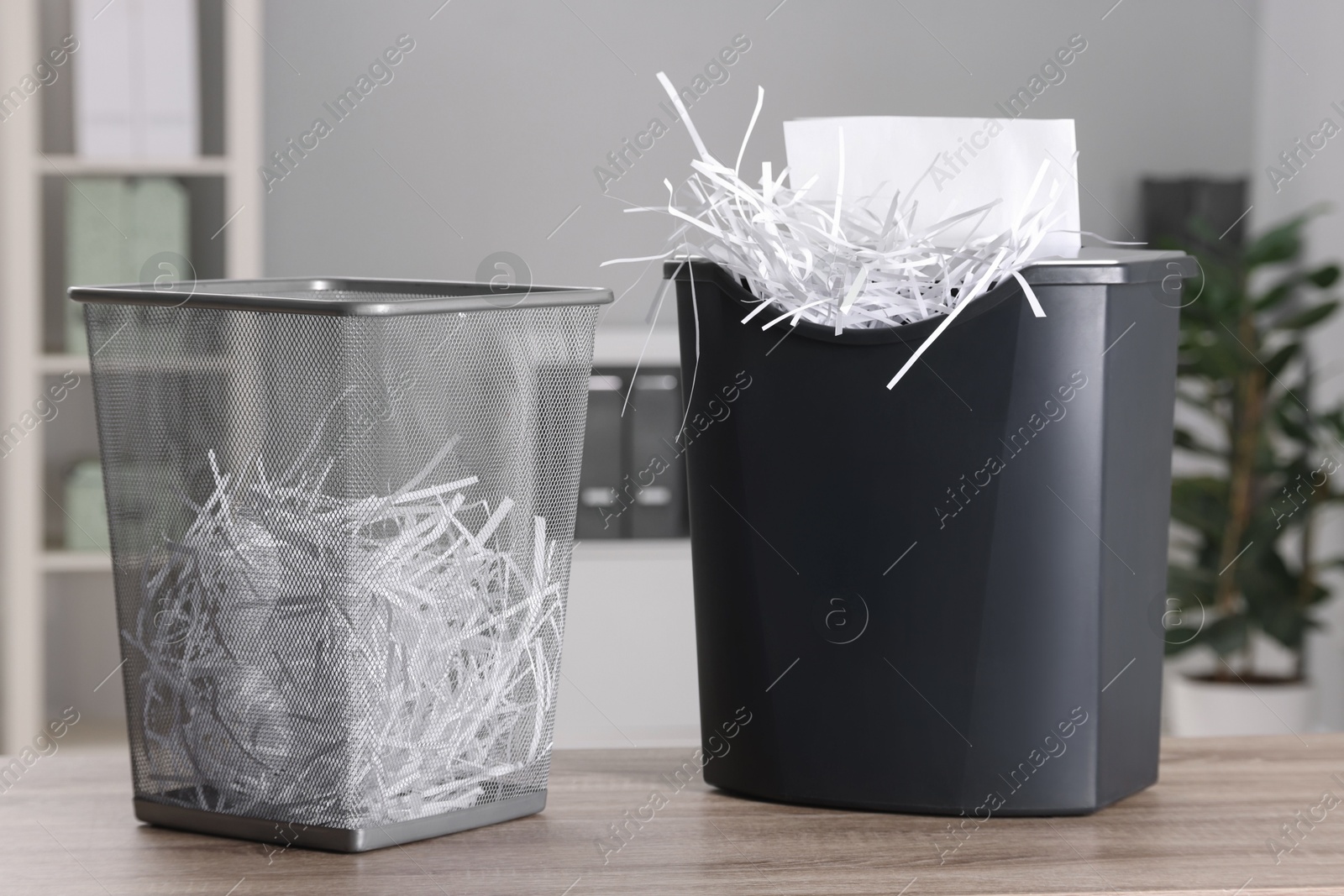 Photo of Destroying sheets with shredder and paper strips in metal bin on wooden table in office