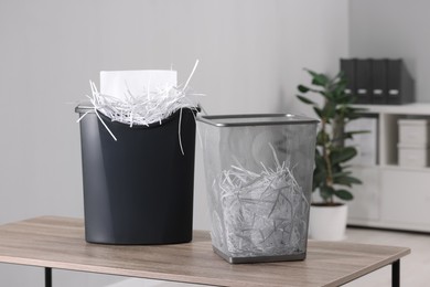 Photo of Destroying sheets with shredder and paper strips in metal bin on wooden table in office