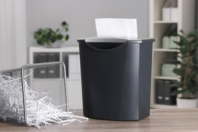 Destroying sheets with shredder and paper strips in metal bin on wooden table in office