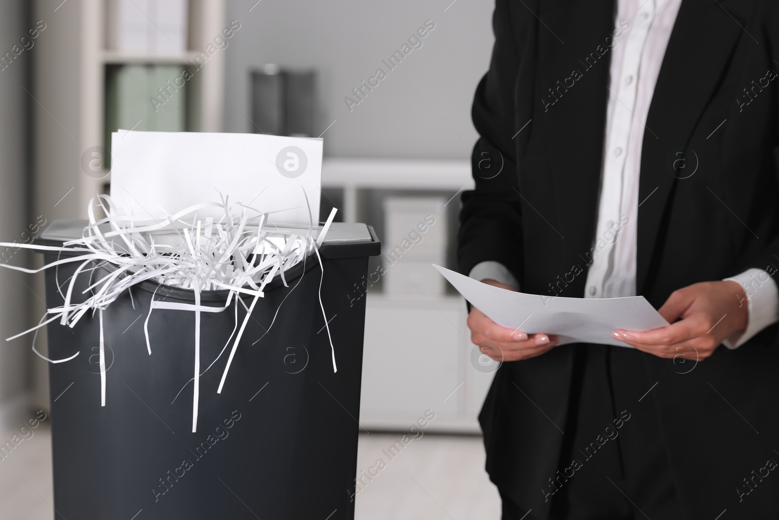 Photo of Woman destroying sheets of paper with shredder in office, closeup