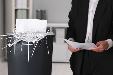 Photo of Woman destroying sheets of paper with shredder in office, closeup