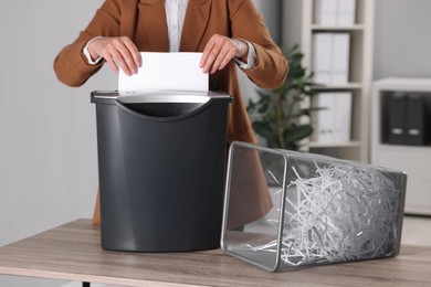 Photo of Woman destroying sheet of paper with shredder at wooden table in office, closeup