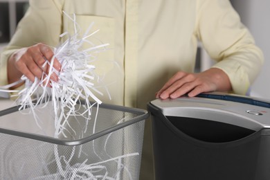 Photo of Woman putting shredded paper strips into trash bin indoors, closeup