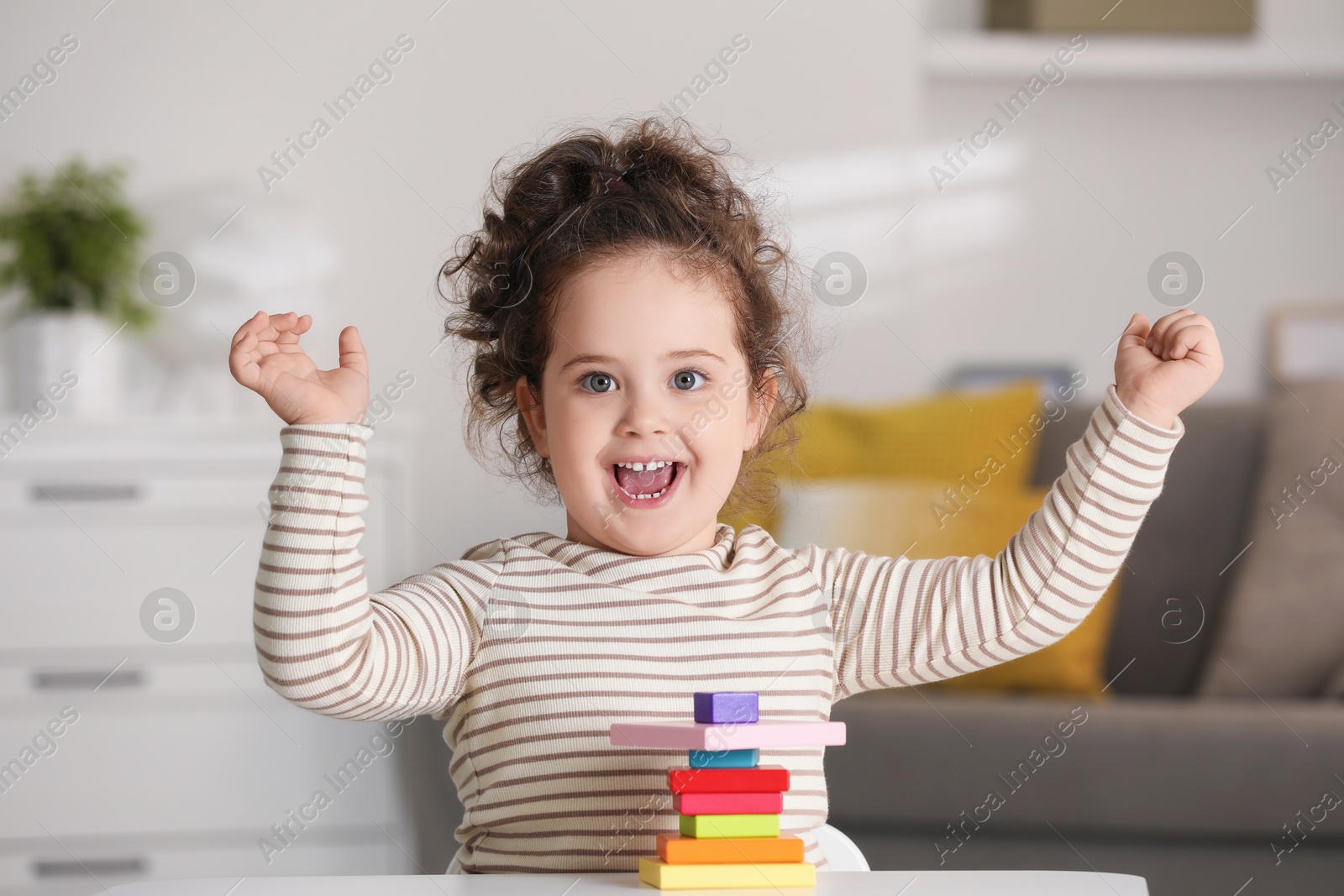 Photo of Portrait of happy girl playing with wooden geometric figures at table indoors. Adorable child