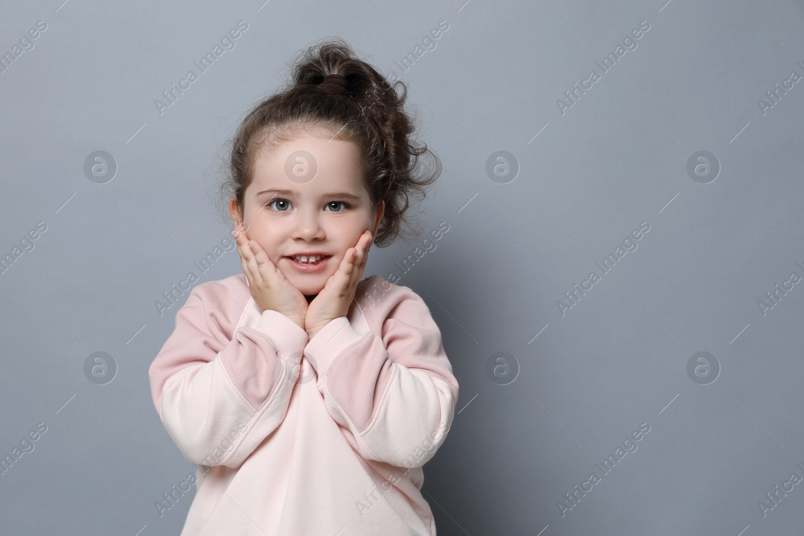 Photo of Adorable child. Portrait of smiling girl on grey background. Space for text