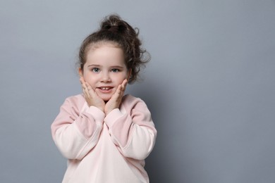 Photo of Adorable child. Portrait of smiling girl on grey background. Space for text