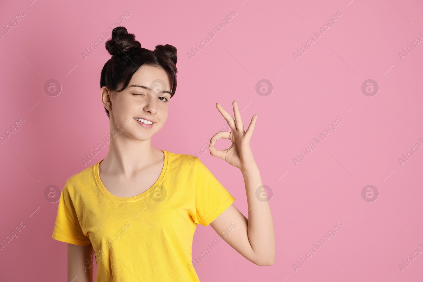 Photo of Portrait of smiling teenage girl showing ok gesture on pink background. Space for text