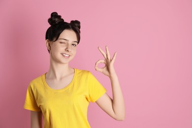 Portrait of smiling teenage girl showing ok gesture on pink background. Space for text