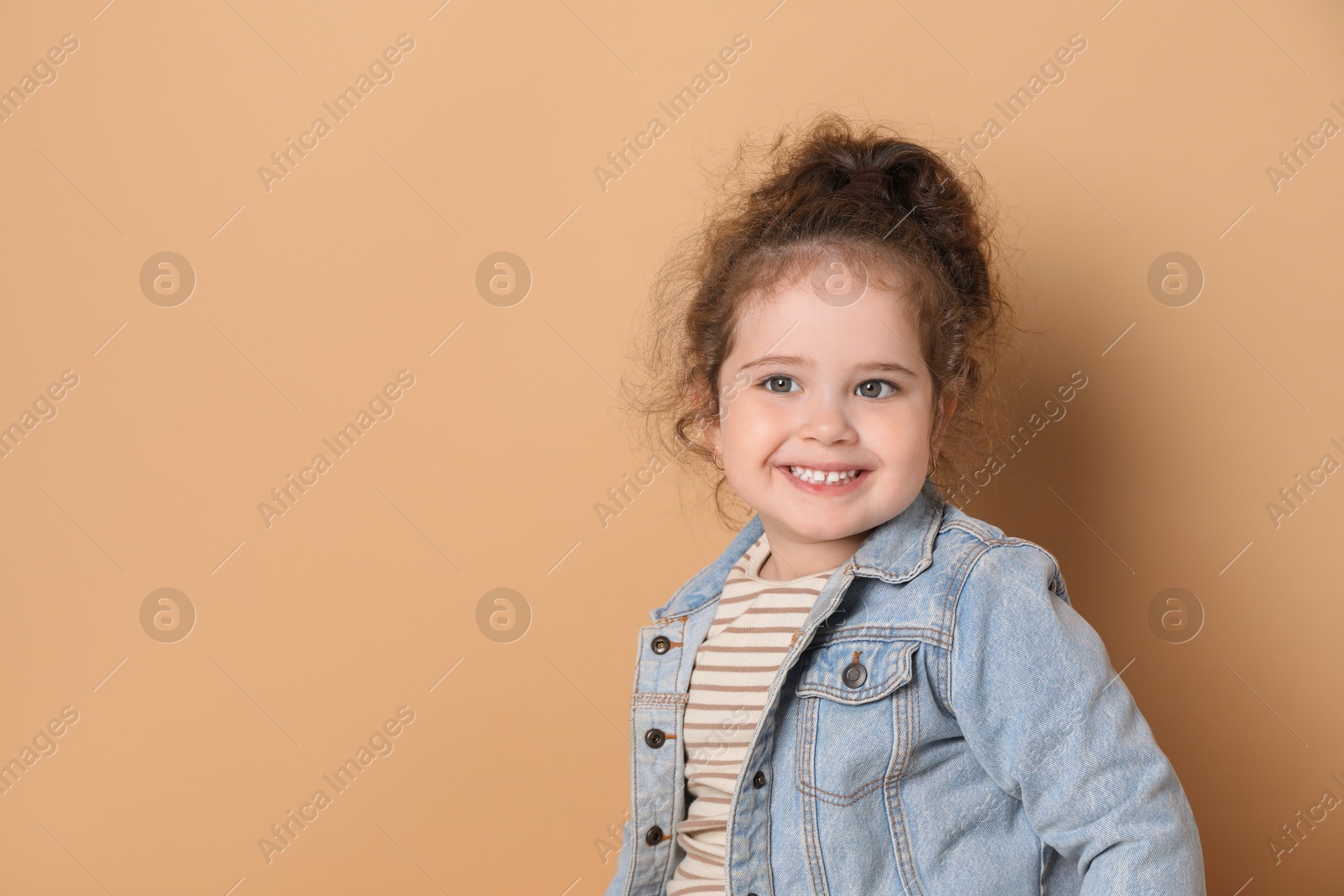 Photo of Adorable child. Portrait of happy girl on beige background, space for text