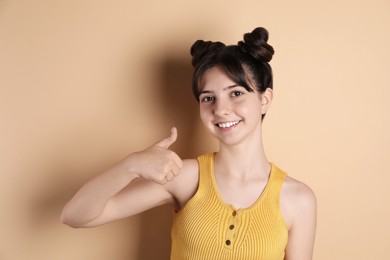 Photo of Portrait of smiling teenage girl showing thumbs up on beige background