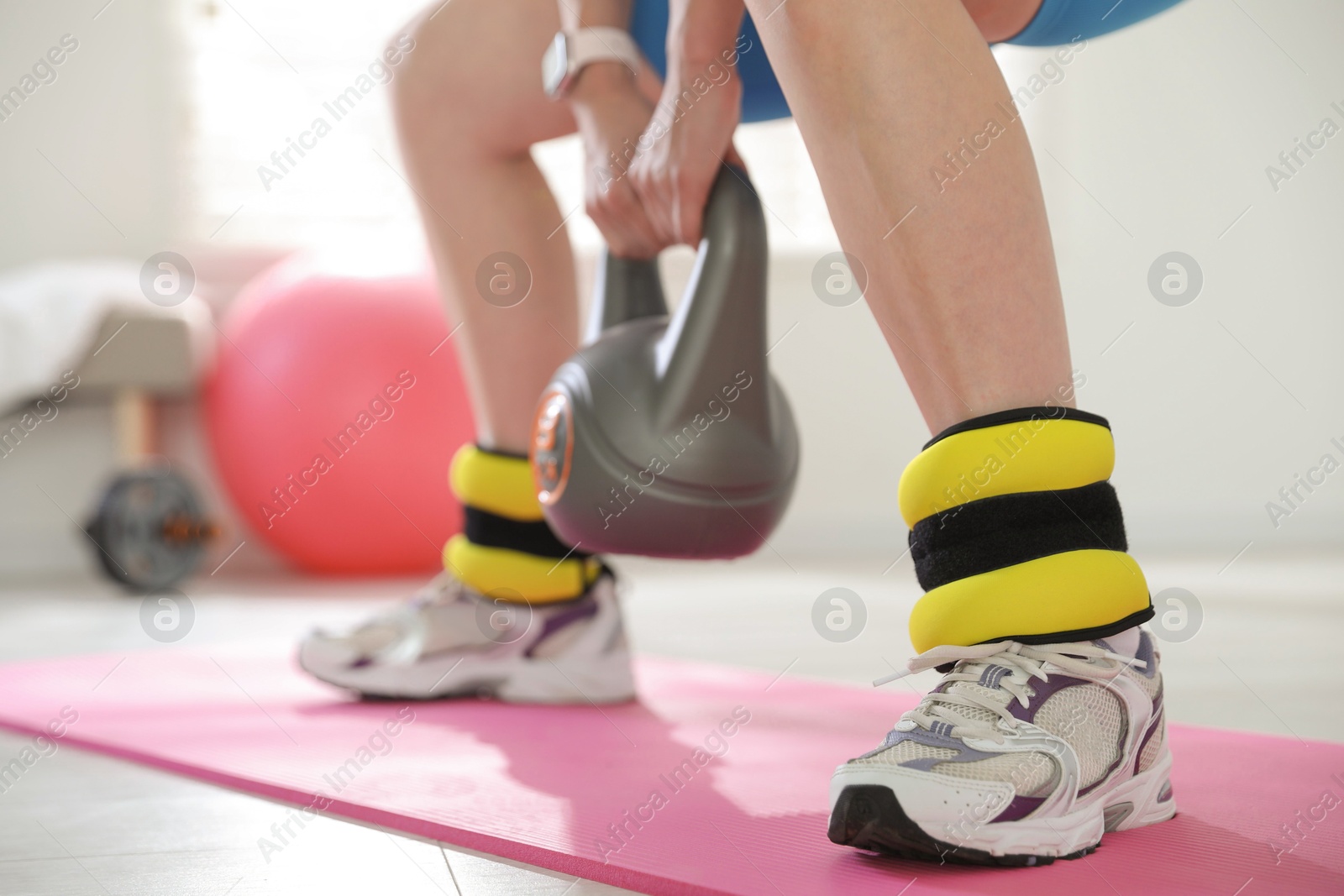 Photo of Beautiful woman with ankle weights and kettlebell training indoors