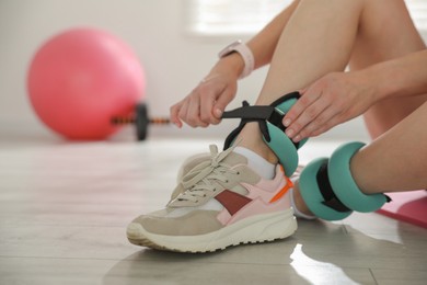 Photo of Beautiful woman putting on ankle weights indoors, closeup