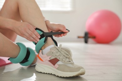 Photo of Beautiful woman putting on ankle weights indoors, closeup