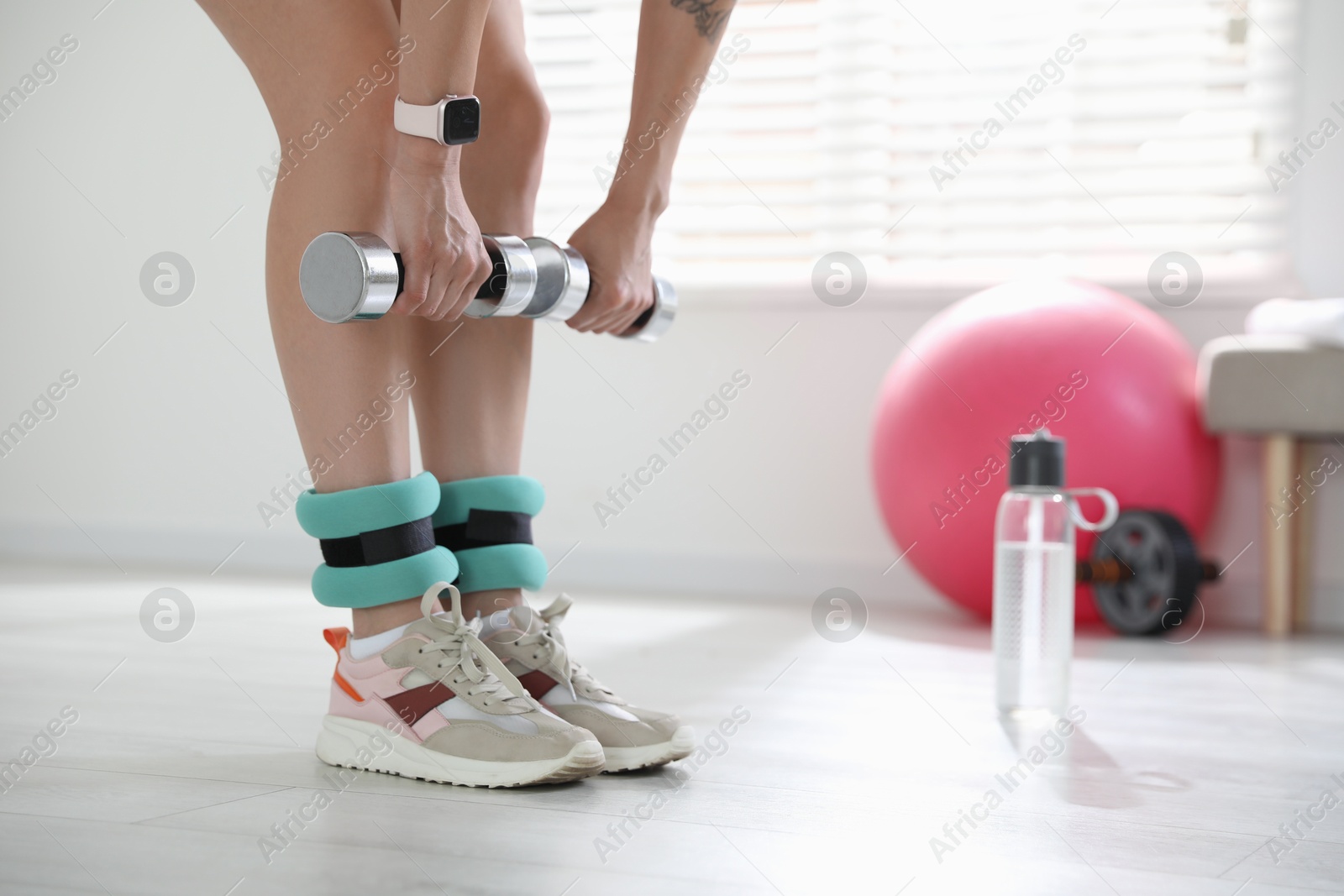 Photo of Woman with ankle weights and dumbbells training indoors, closeup