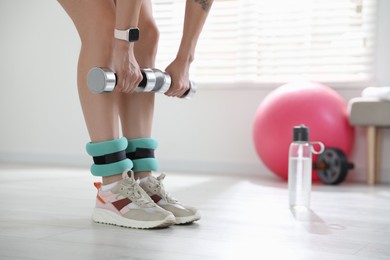 Photo of Woman with ankle weights and dumbbells training indoors, closeup