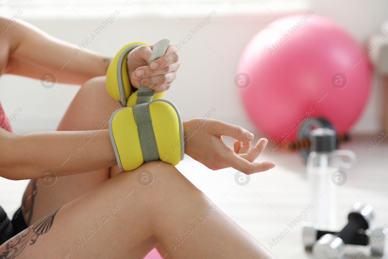 Photo of Woman putting ankle weight on her arm indoors, closeup