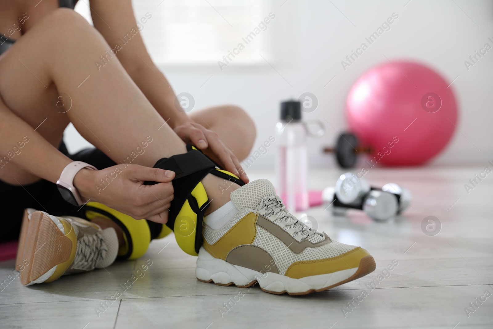 Photo of Woman putting on ankle weights indoors, closeup