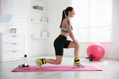 Beautiful woman with ankle weights doing exercises indoors