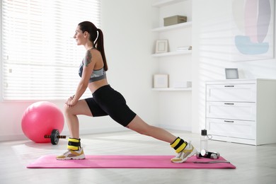 Beautiful woman with ankle weights doing exercises indoors