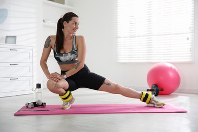 Beautiful woman with ankle weights doing exercises indoors