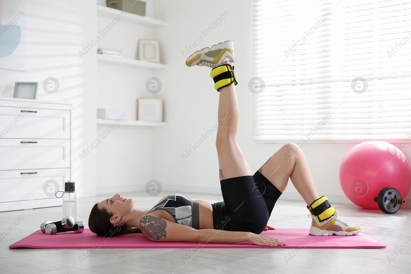 Photo of Beautiful woman with ankle weights doing exercises indoors