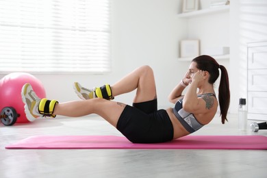 Photo of Beautiful woman with ankle weights doing exercises indoors