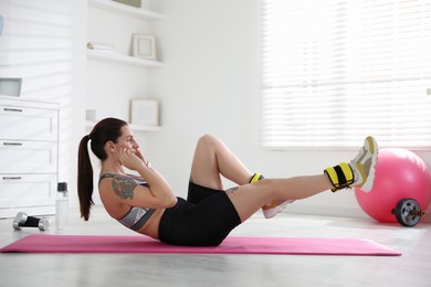 Photo of Beautiful woman with ankle weights doing exercises indoors