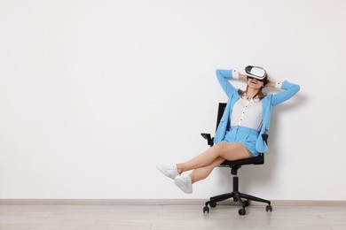 Happy woman with virtual reality headset sitting on chair indoors, space for text