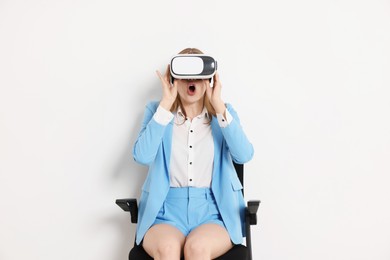 Emotional woman with virtual reality headset sitting on chair against white background