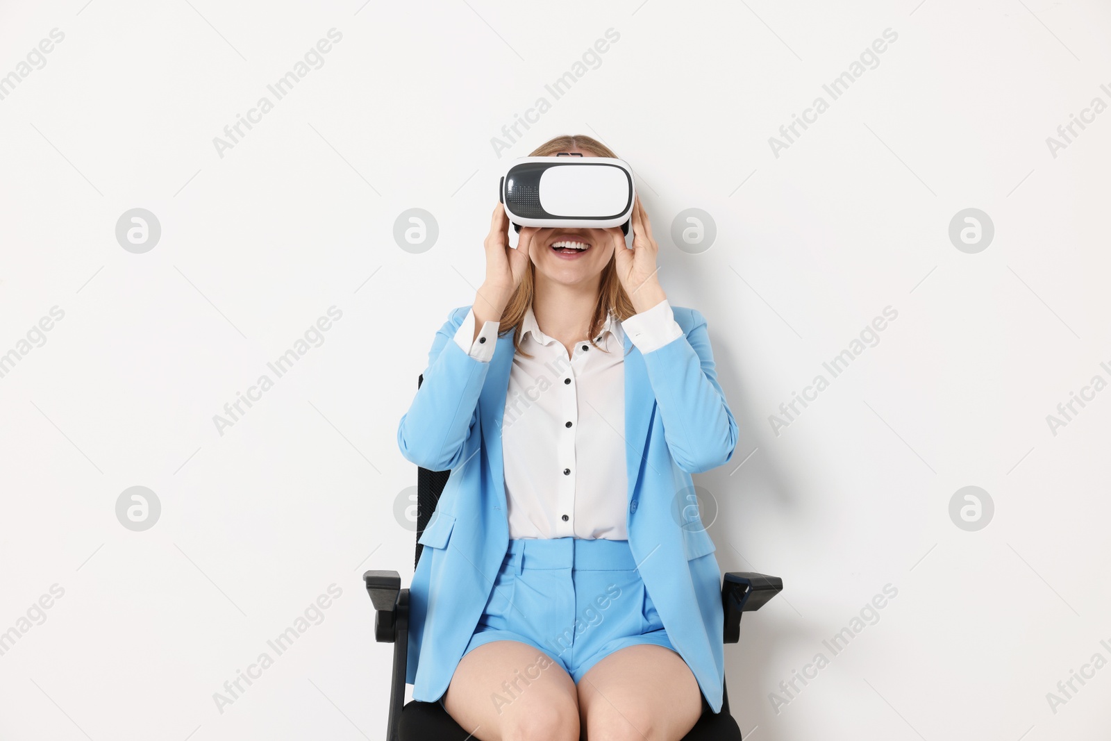 Photo of Happy woman with virtual reality headset sitting on chair against white background