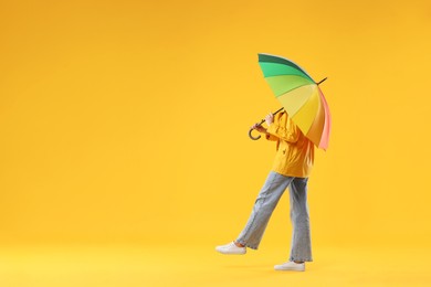 Photo of Woman with colorful umbrella on yellow background, space for text