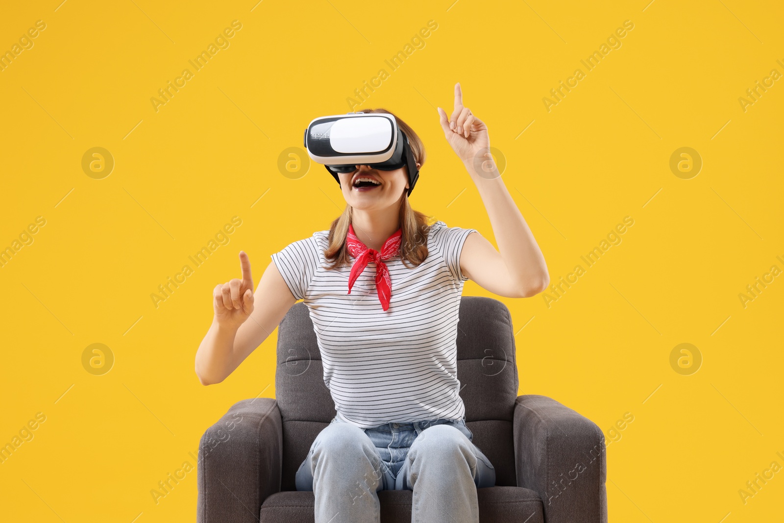 Photo of Happy woman with virtual reality headset sitting in armchair on yellow background