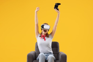 Happy woman with virtual reality headset and controller sitting in armchair on yellow background