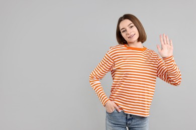 Happy teenage girl waving on gray background, space for text