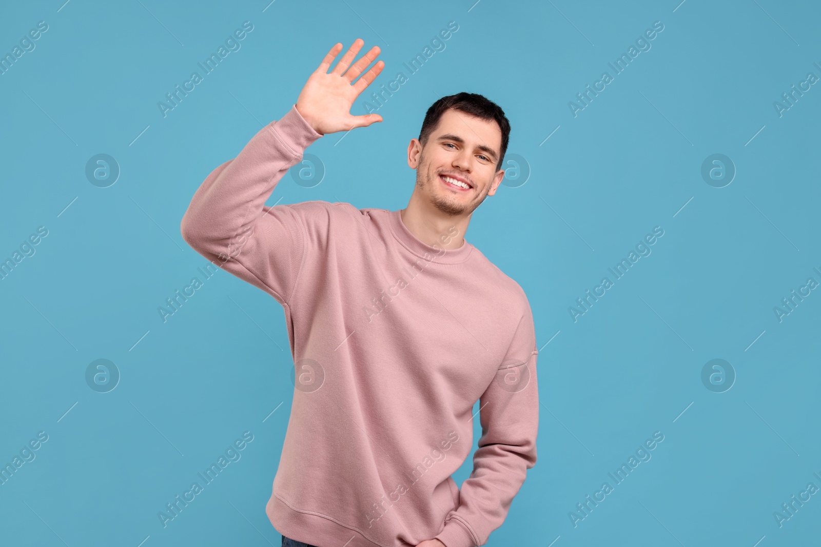 Photo of Happy young man waving on light blue background