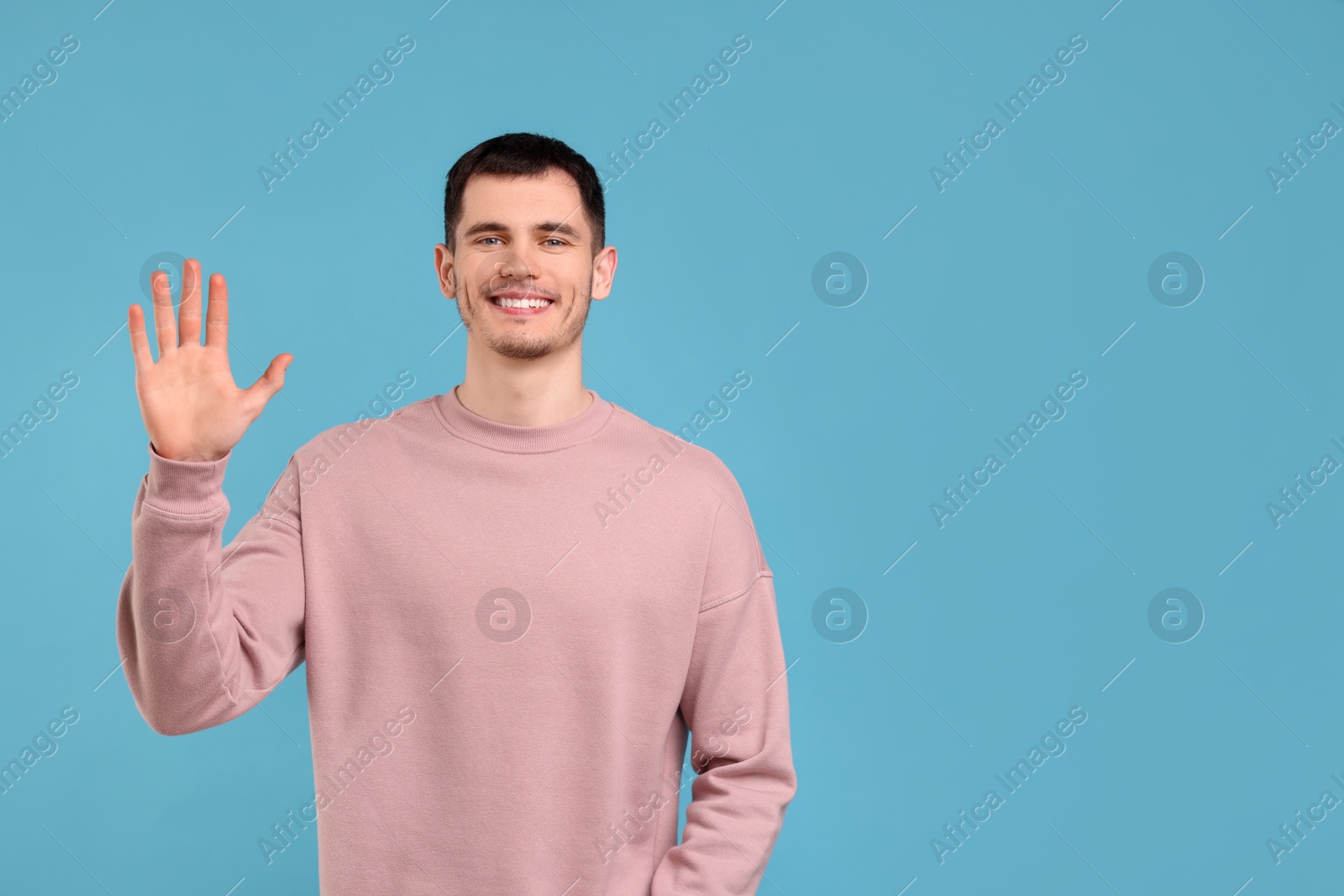 Photo of Happy young man waving on light blue background, space for text