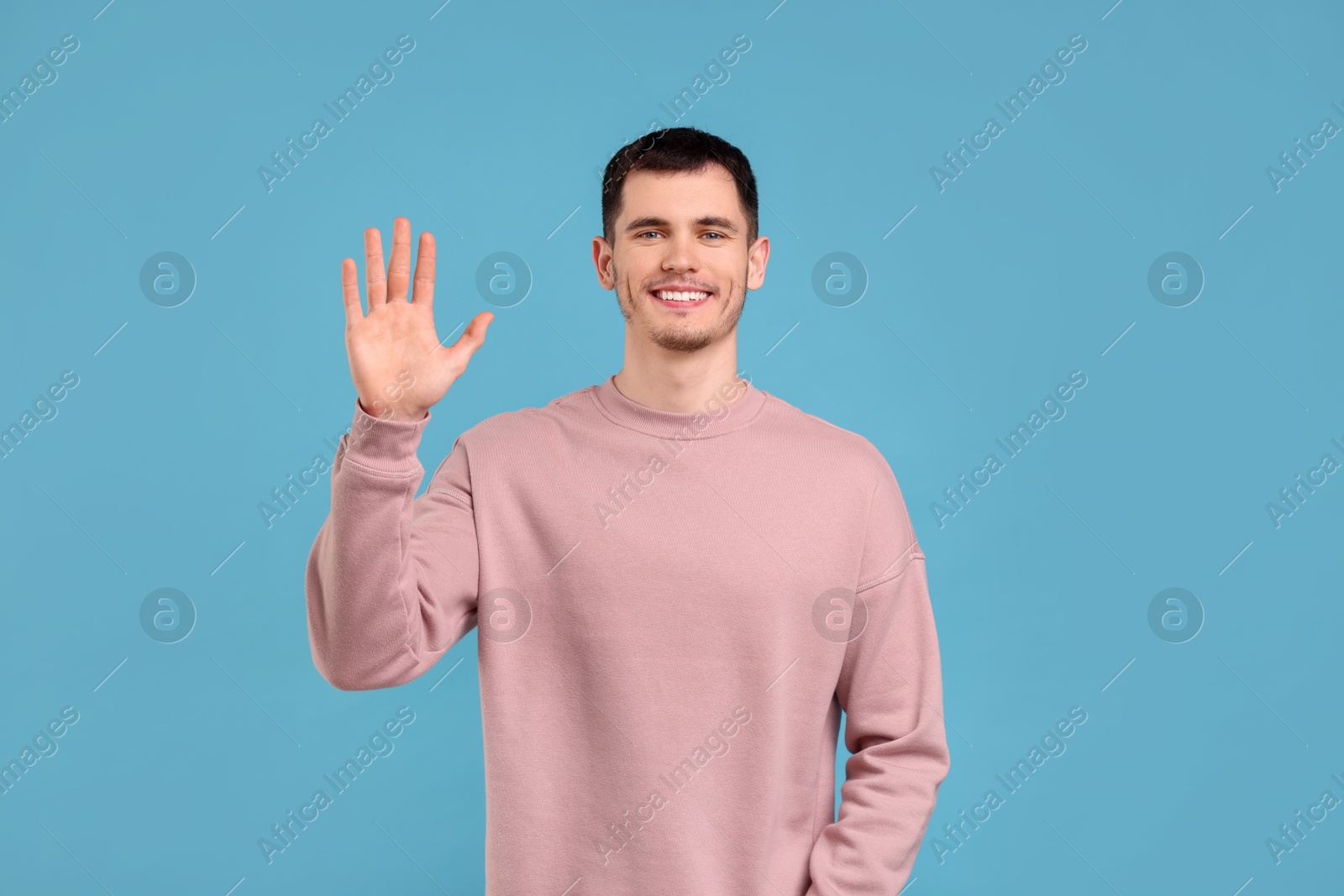 Photo of Happy young man waving on light blue background