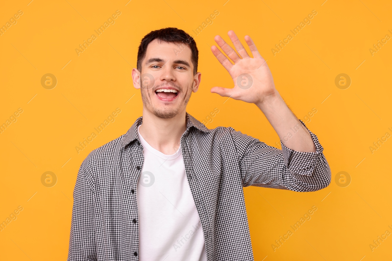 Photo of Happy young man waving on orange background