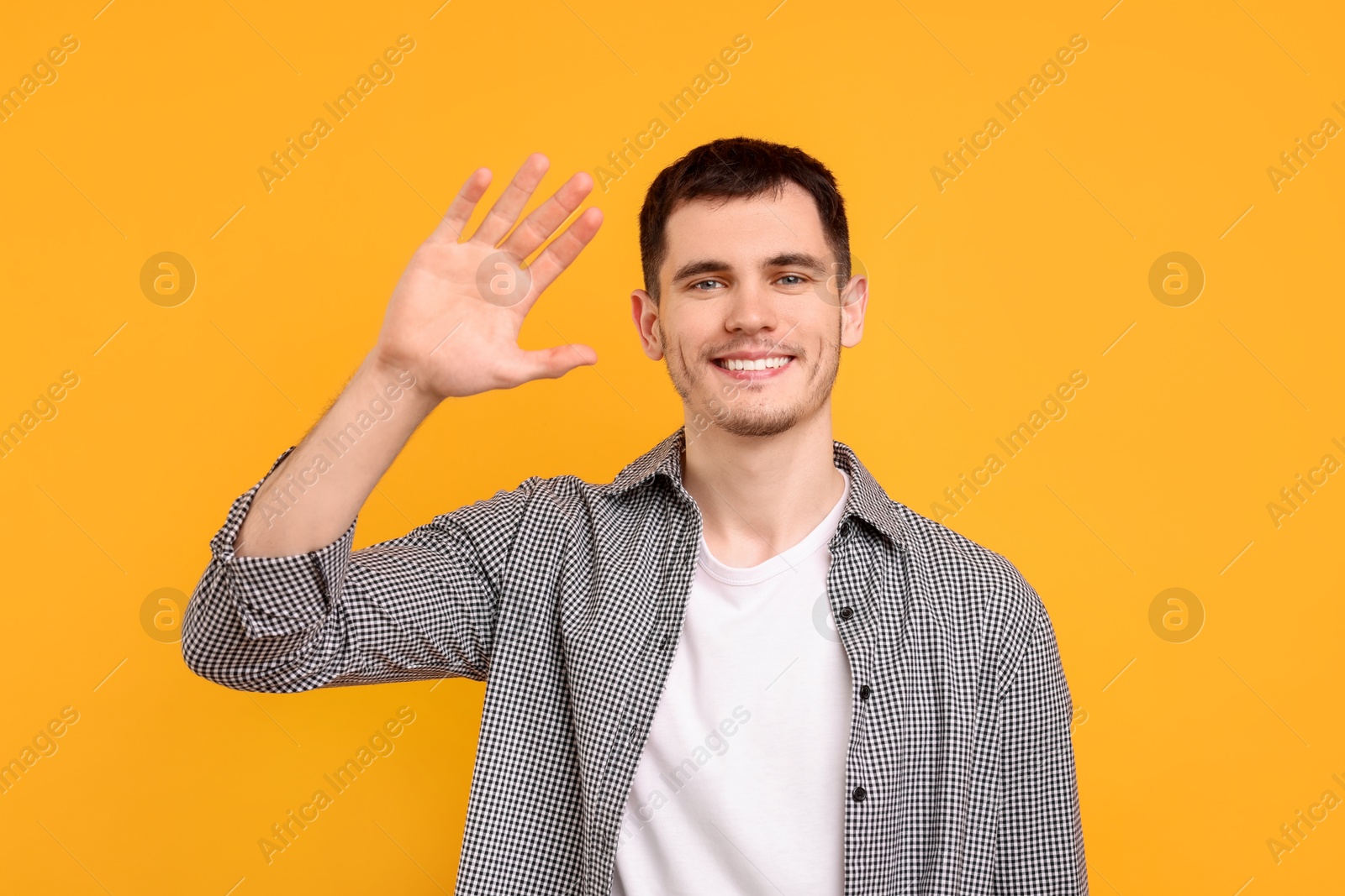 Photo of Happy young man waving on orange background