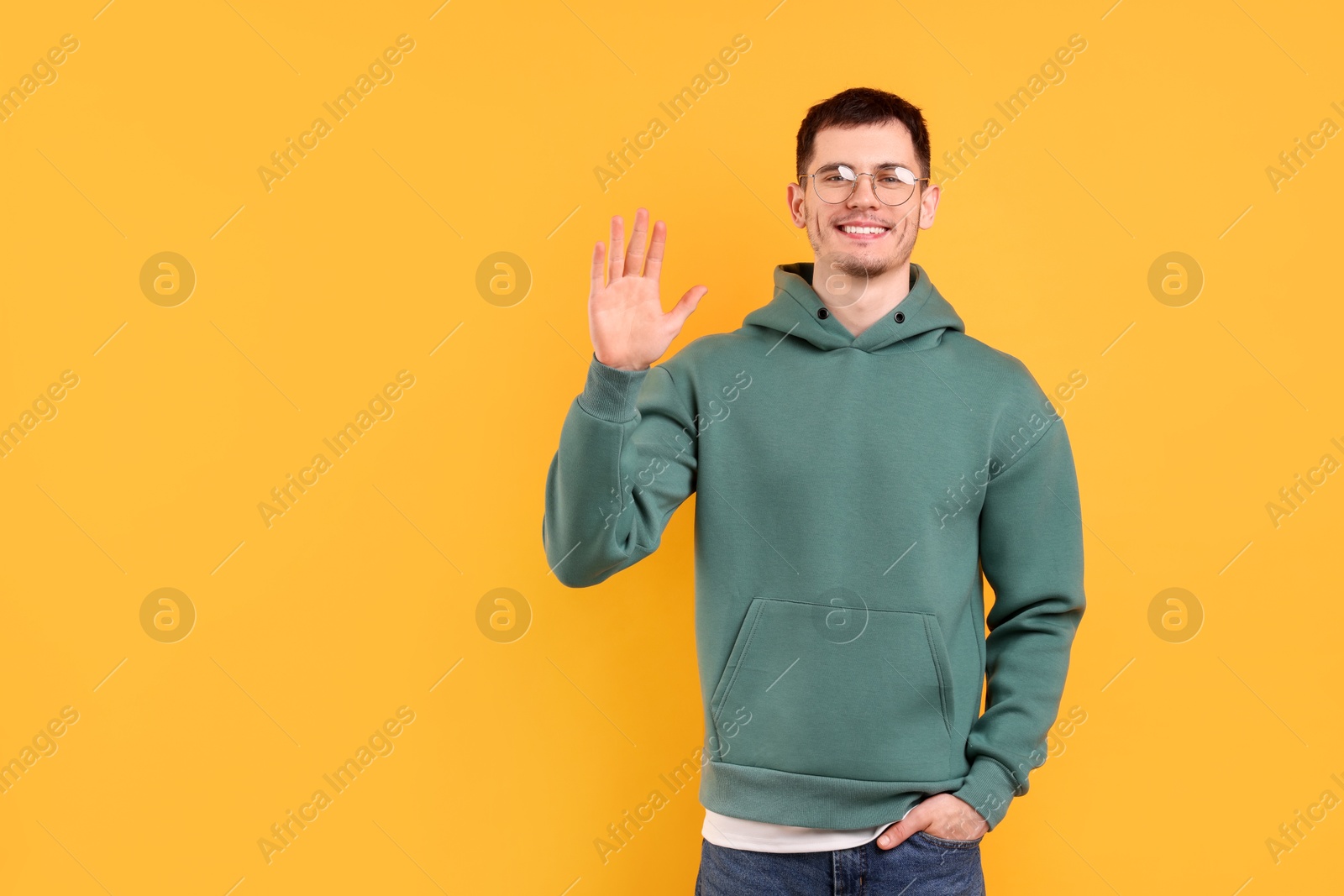 Photo of Happy young man waving on orange background, space for text