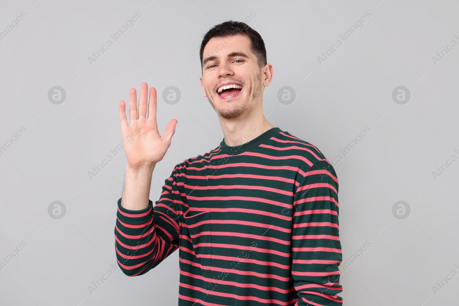 Photo of Happy young man waving on gray background