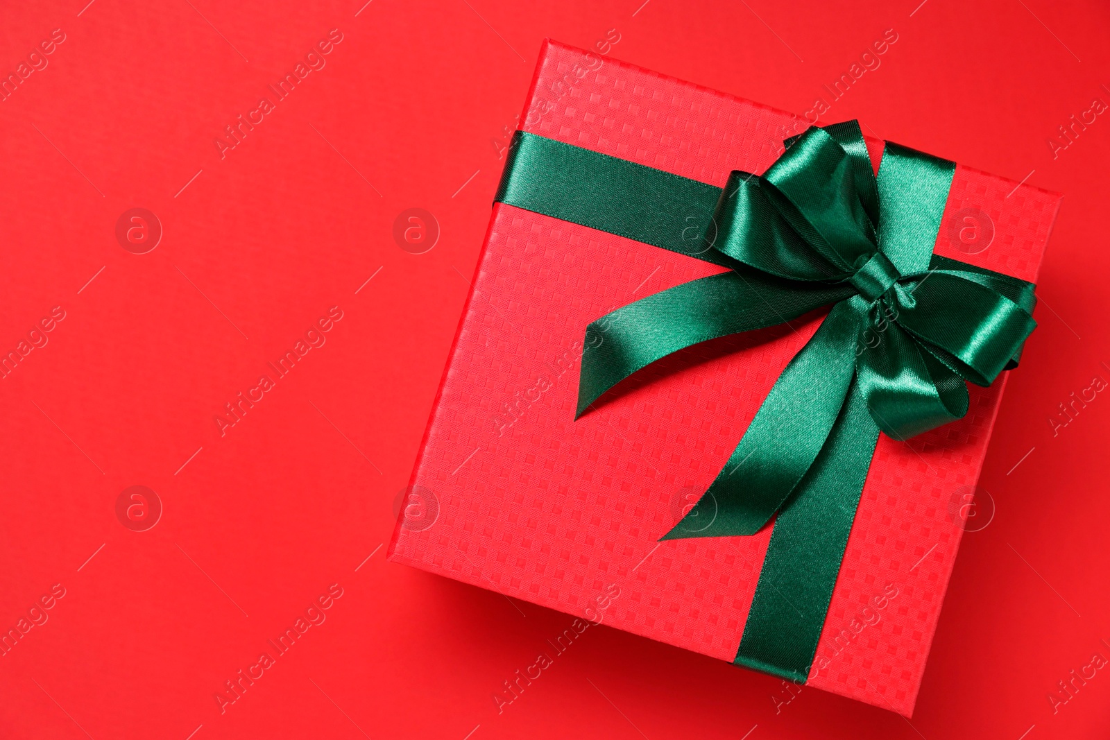 Photo of Gift box with green bow on red background, top view. Space for text