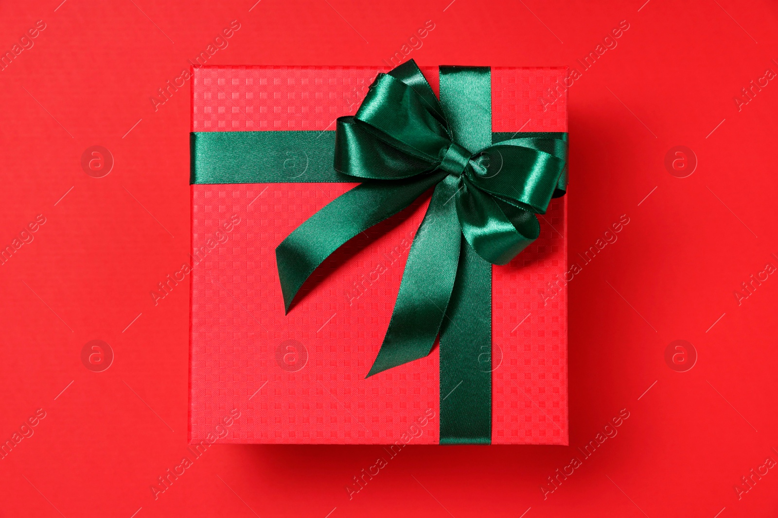 Photo of Gift box with green bow on red background, top view