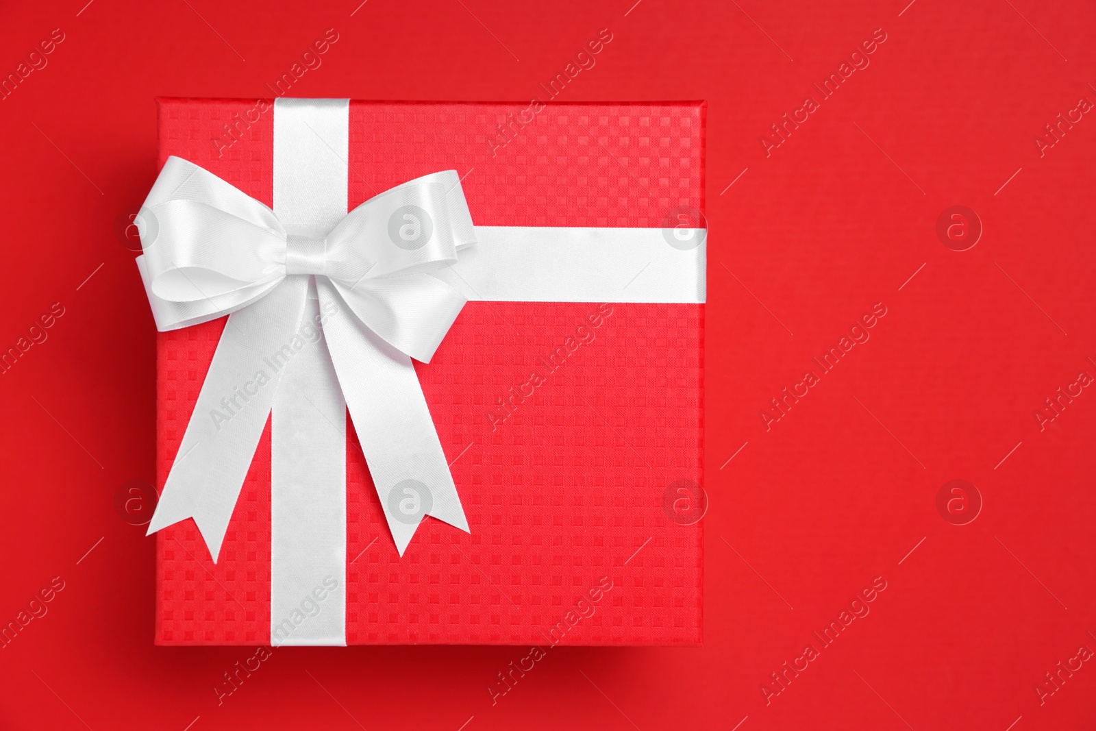 Photo of Gift box with white bow on red background, top view. Space for text