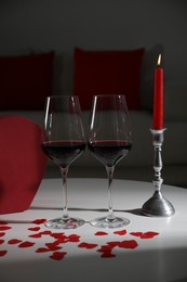 Burning candle, wine in glasses and paper hearts on table indoors