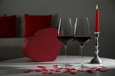 Burning candle, wine in glasses and paper hearts on table indoors