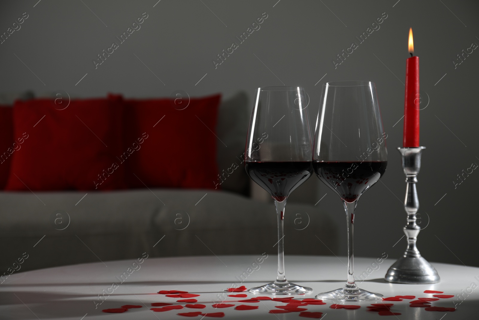 Photo of Burning candle, wine in glasses and paper hearts on table indoors. Space for text