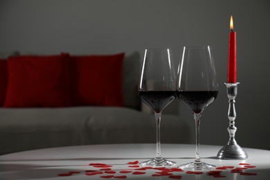 Burning candle, wine in glasses and paper hearts on table indoors. Space for text