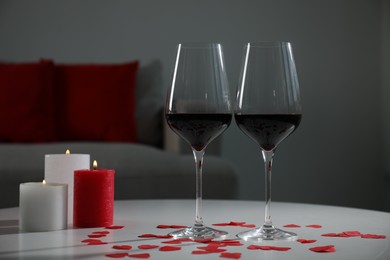 Burning candles, wine in glasses and paper hearts on table indoors