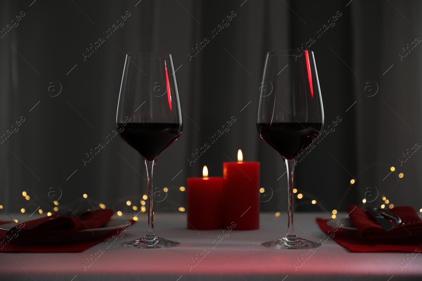 Photo of Burning candles and wine in glasses on table indoors. Bokeh effect